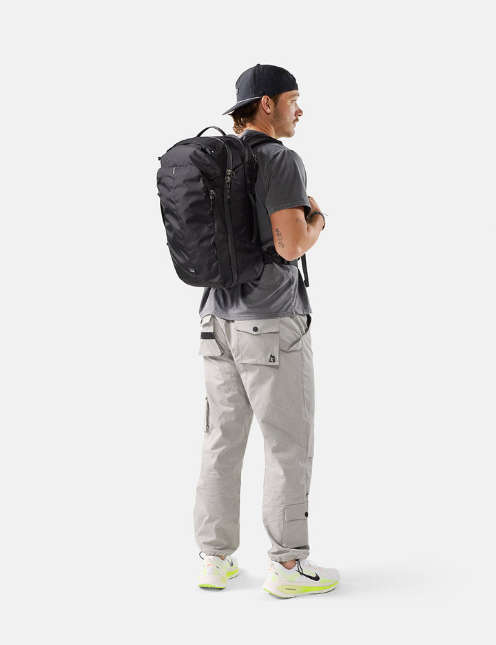 Matador 30L Carry-On Travel Pack in Black - person wearing a black backpack and gray pants on a white background