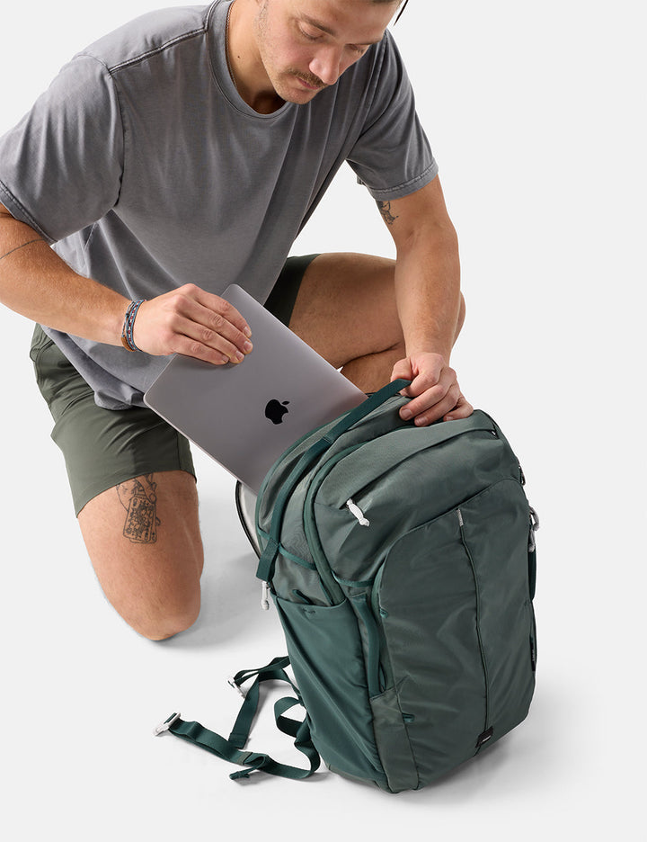 Matador 30L Carry-On Travel Pack in Juniper - man placing a laptop into a green backpack on a white background