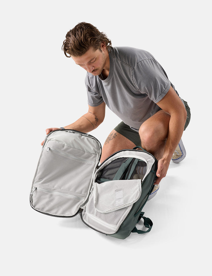 Matador 30L Carry-On Travel Pack in Juniper - man unpacking a juniper backpack on a white background