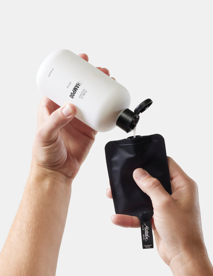 Matador FlatPak™ Toiletry Bottles - 3 Pack (Multi-Colour) - person pouring liquid from a white bottle with a black nozzle into a black pouch on a light gray background