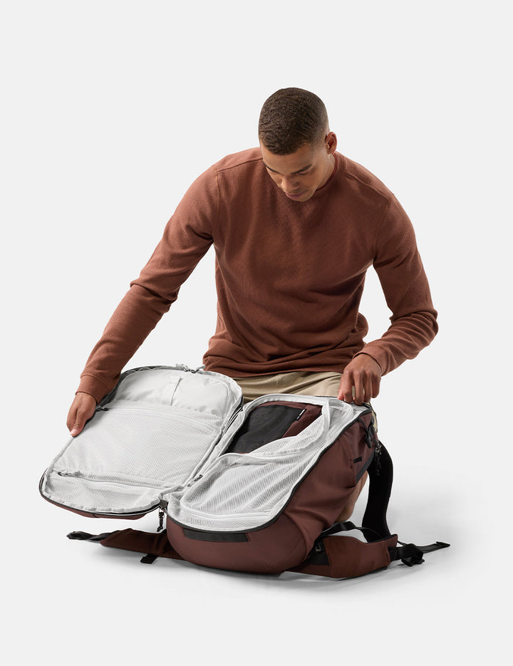 Matador 35L Global Travel Pack in Garnet - man opening a garnet backpack with a clear compartment on a white background