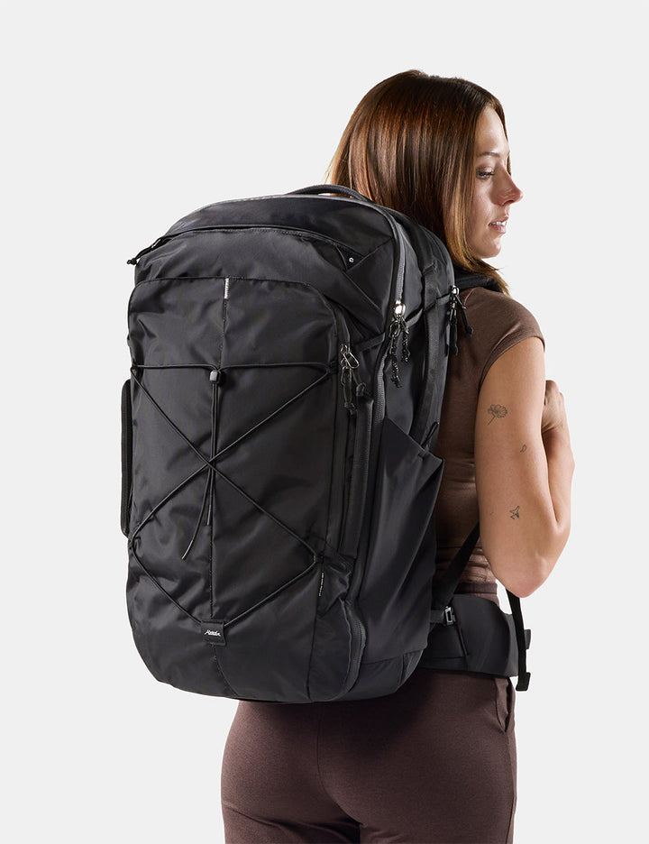 Matador 45L Global Travel Pack in Black - a woman shown from the back wearing a large black backpack against a light gray studio background