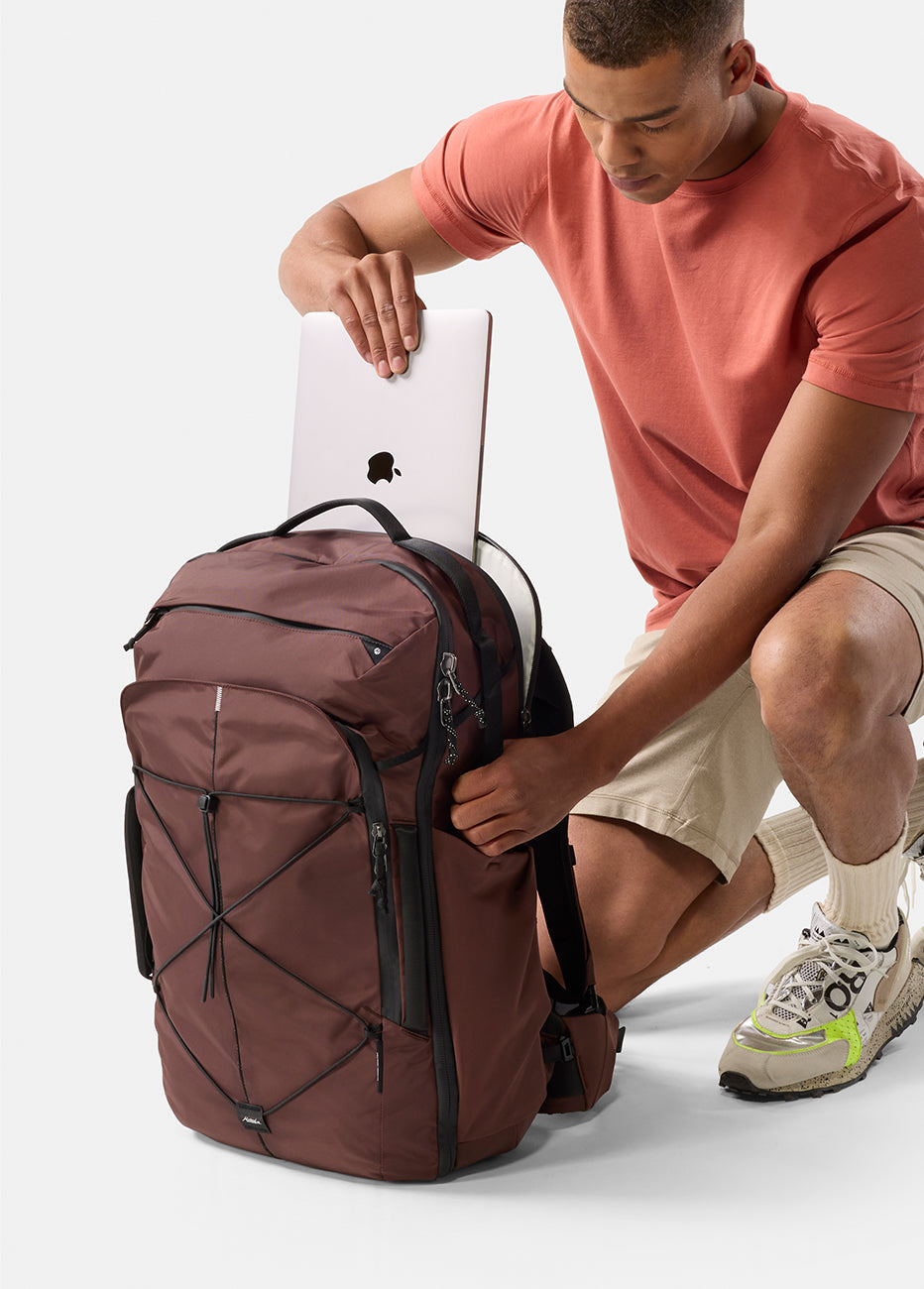 Matador 45L Global Travel Pack in Garnet - man placing a laptop into a garnet backpack on a white background