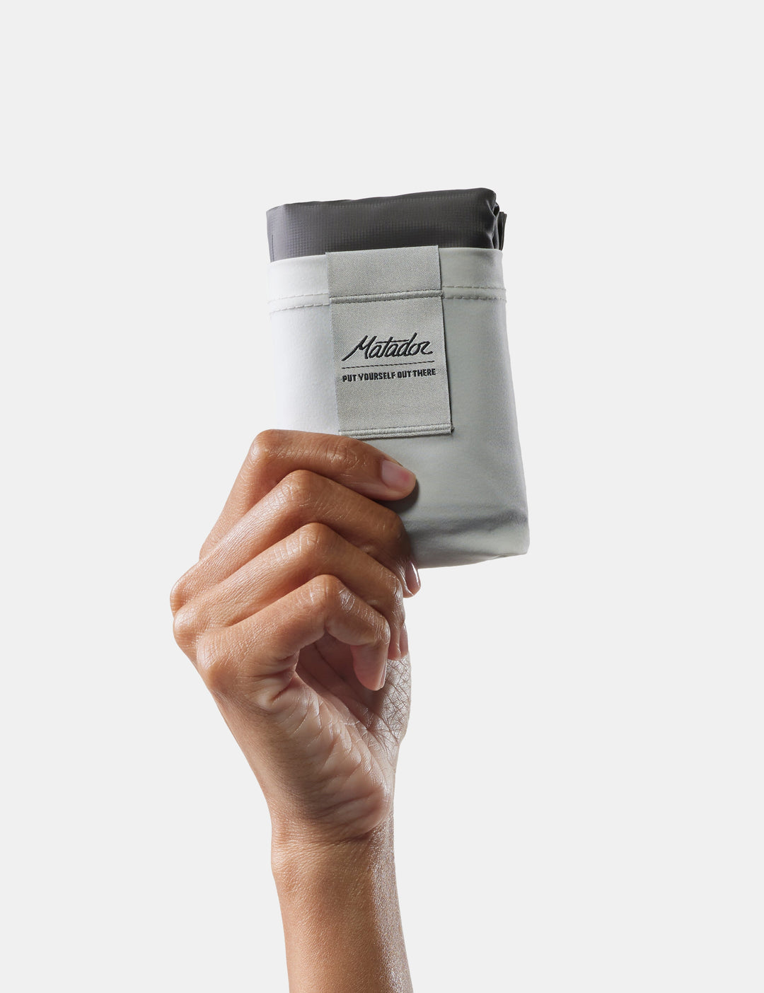 Matador Pocket Blanket™ 4.0 - 160 x 110cm in Ghost Grey - hand holding a white pocket blanket on a light gray background