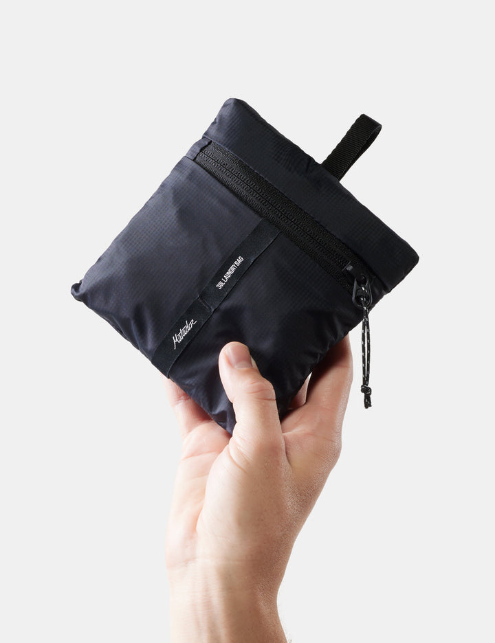 Matador Packable Laundry Bag - hand holding a black pouch with a visible brand logo on a white background