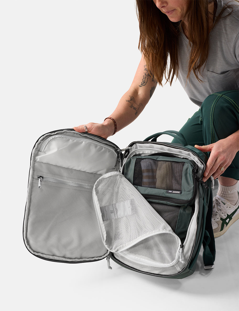 Matador 18L Personal Item Travel Pack in Juniper - person opening a green travel backpack with a clear front pocket on a white background