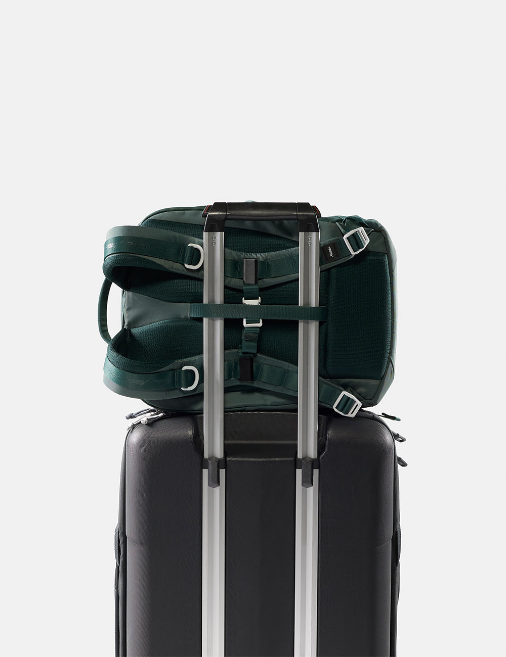 Matador 18L Personal Item Travel Pack in Juniper - green backpack attached to a black suitcase on a light gray background
