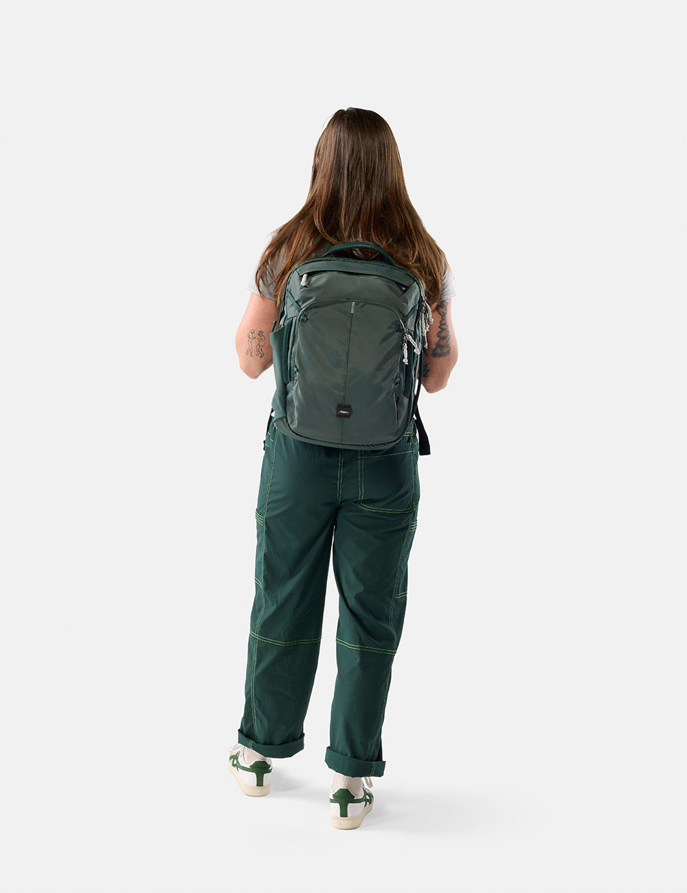 Matador 18L Personal Item Travel Pack in Juniper - person wearing a green backpack and green pants on a white background