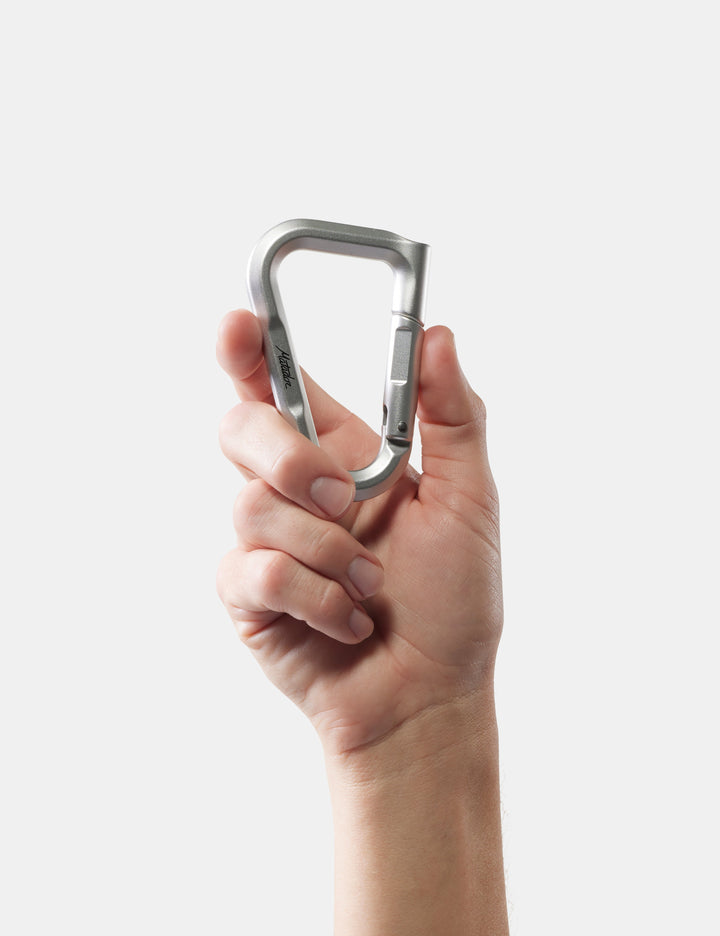 Matador BetaLock in Canyon Orange - hand holding a metallic carabiner against a white background