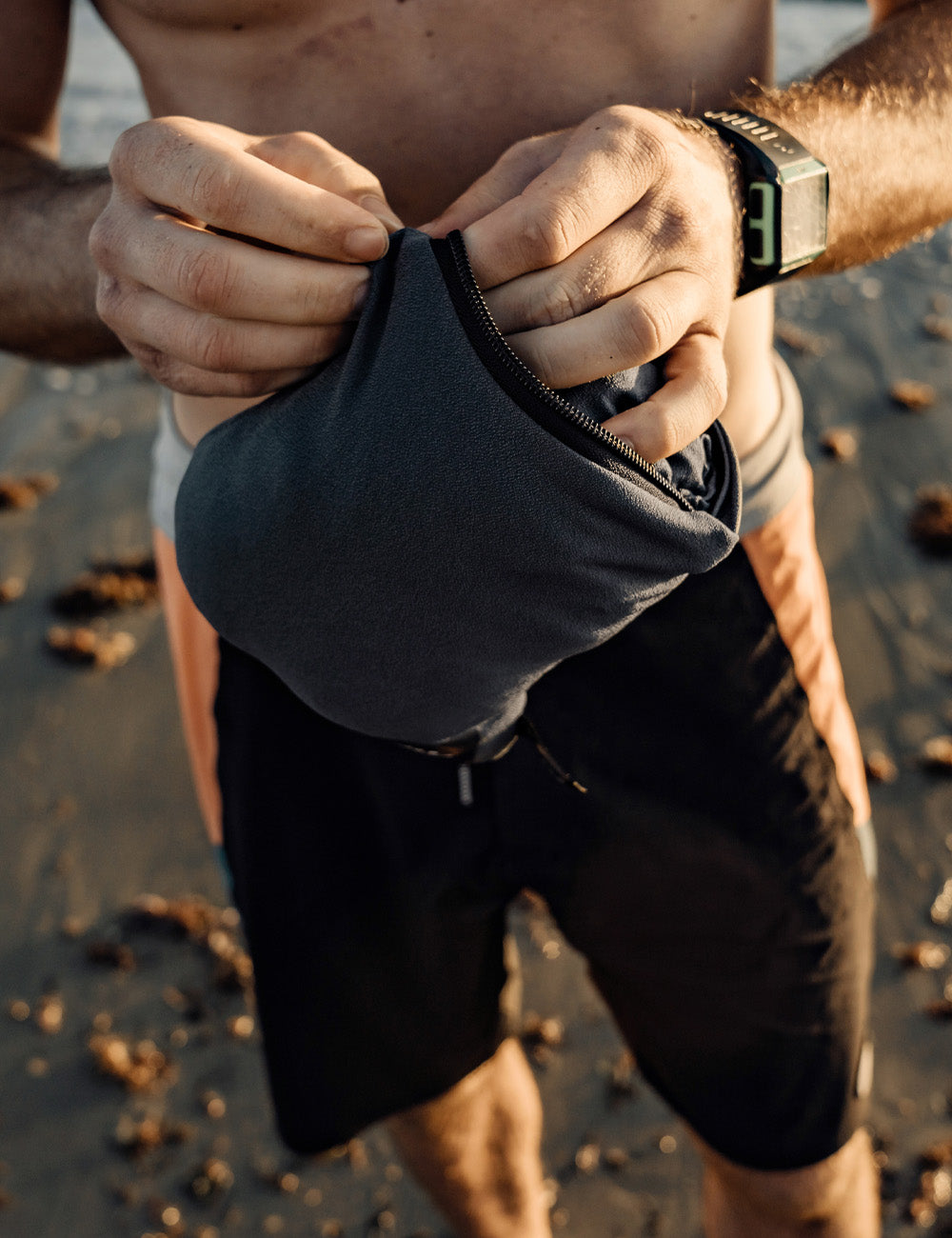 Matador NanoDry™ Packable Towel Poncho in Charcoal - person on a beach holding a black pouch with a watch on their wrist