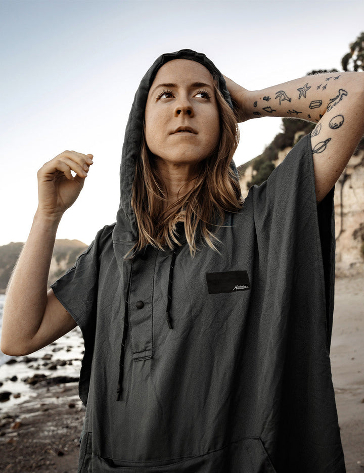 Matador NanoDry™ Packable Towel Poncho in Slate Blue - person wearing a gray poncho with a brand logo on a beach